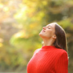 A woman in a red jumper breathing deeply in a woodland setting