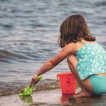 little girl at beach with bucket and spade at water's edge
