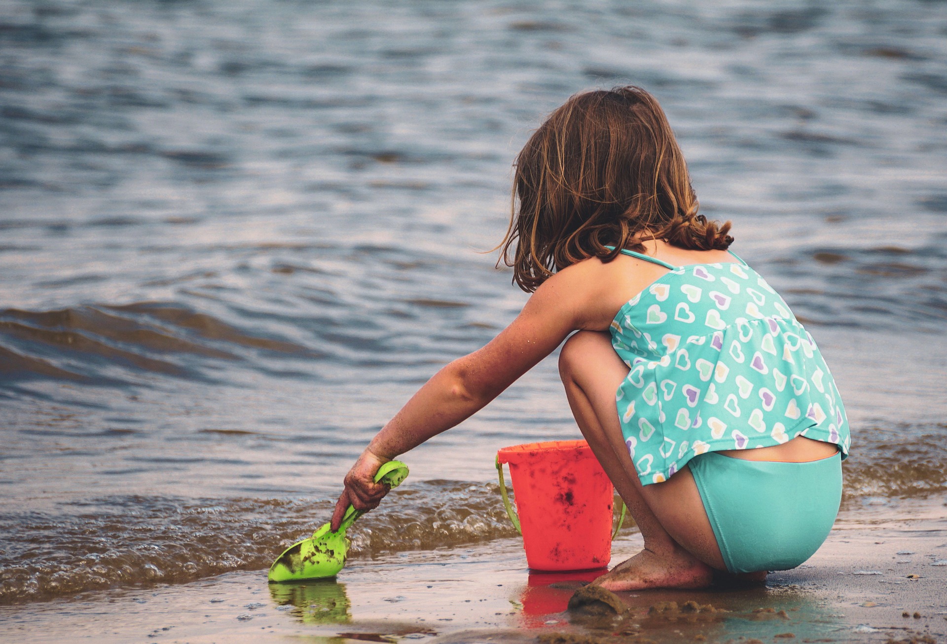 little girl at beach with bucket and spade at water's edge
