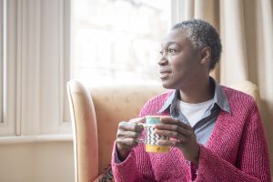 mature woman looking out of the window holding a coffee